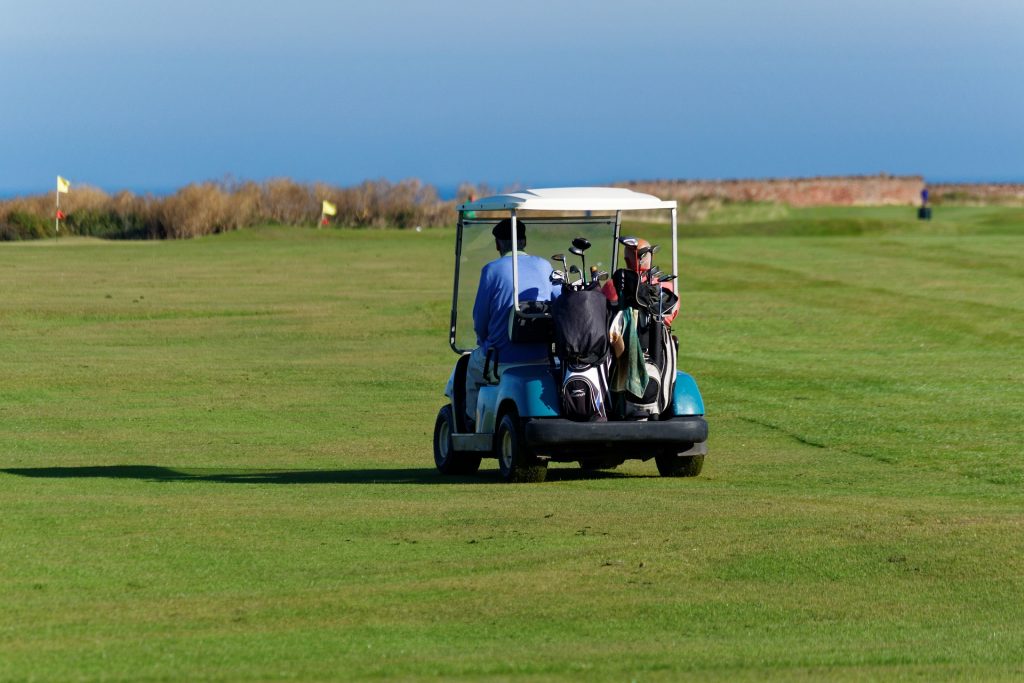 Two work colleagues sharing an electric golf buggy trip across the grass.