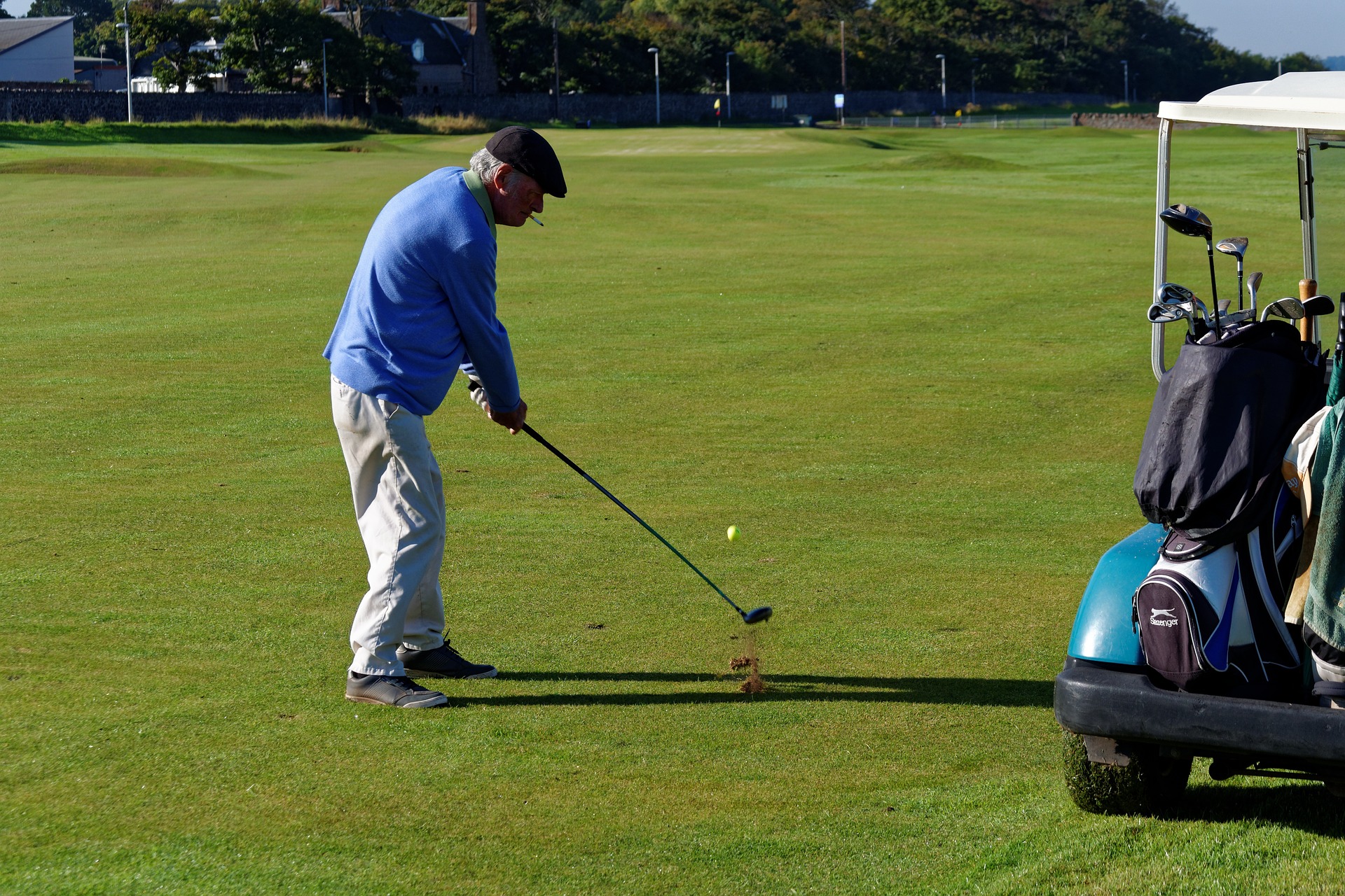 Man playing golf with his electric golf buggy parked up nearby.